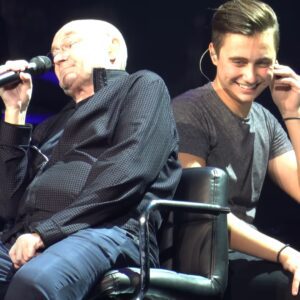 In a darkened stadium in Houston in 2019, Phil Collins took a seat on a piano stool next to his son, Nic Collins. In a humorous exchange, Phil explained that when he showed Nic his music, there had been “just one” song that jiji